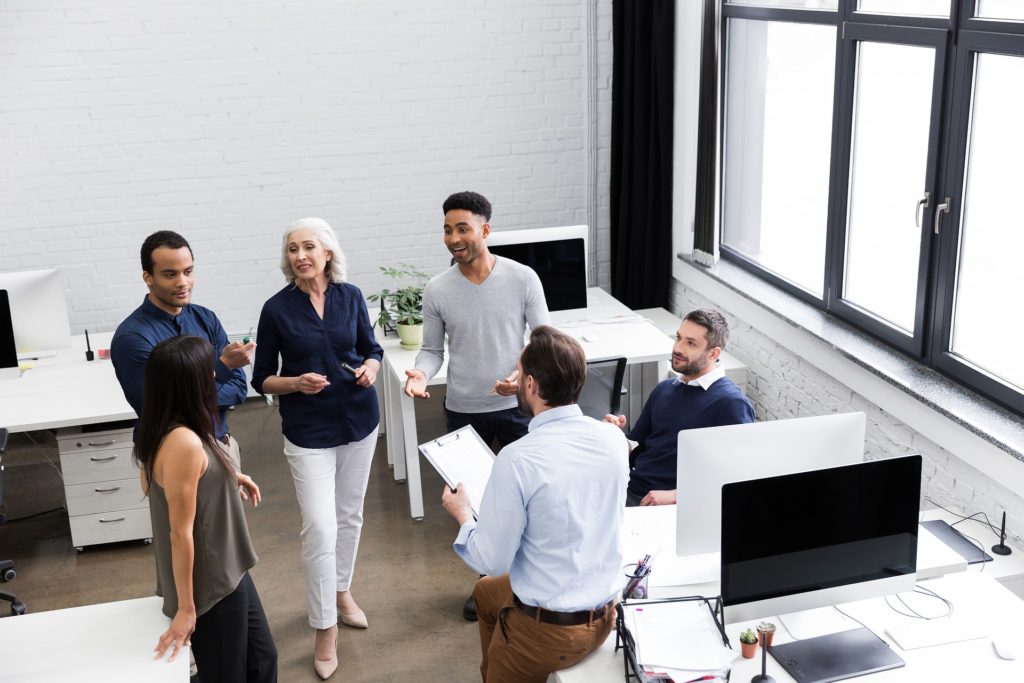 A diverse group of people talking in a white-walled office environment.